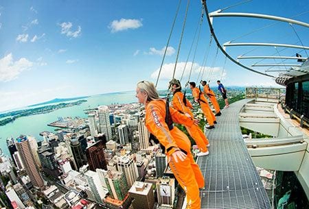 Tourists in harnesses leaning out from the Skywalk platform at the top of the Sky Tower building